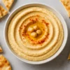 Bol de houmous crémeux préparé au Thermomix, garni de pois chiches, paprika et huile d’olive, servi avec du pain pita.